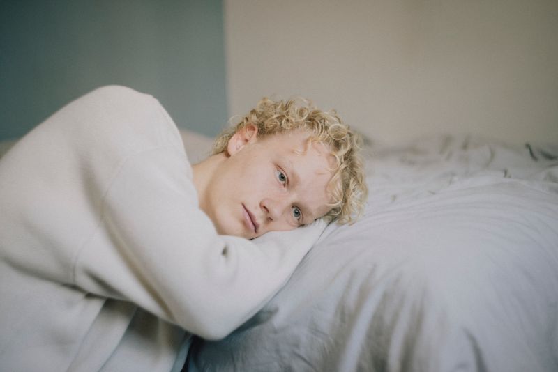 En dreng ligger med hovedet på sengen og stirrer tomt ud i luften