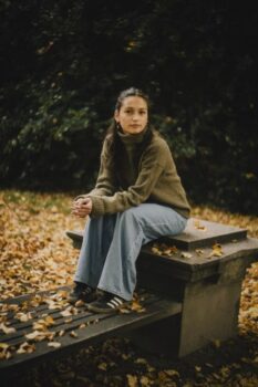 Paula sidder på en bænk i en park og kigger ind i kameraet