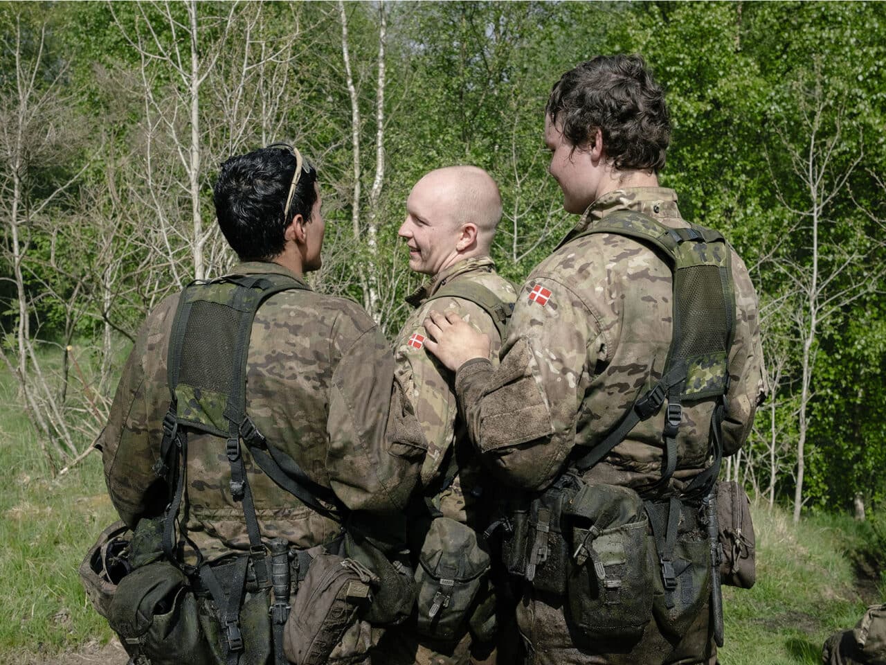 En gruppe soldater står sammen i en skov. Den ene har hånden på den andens skulder. De ser glade ud