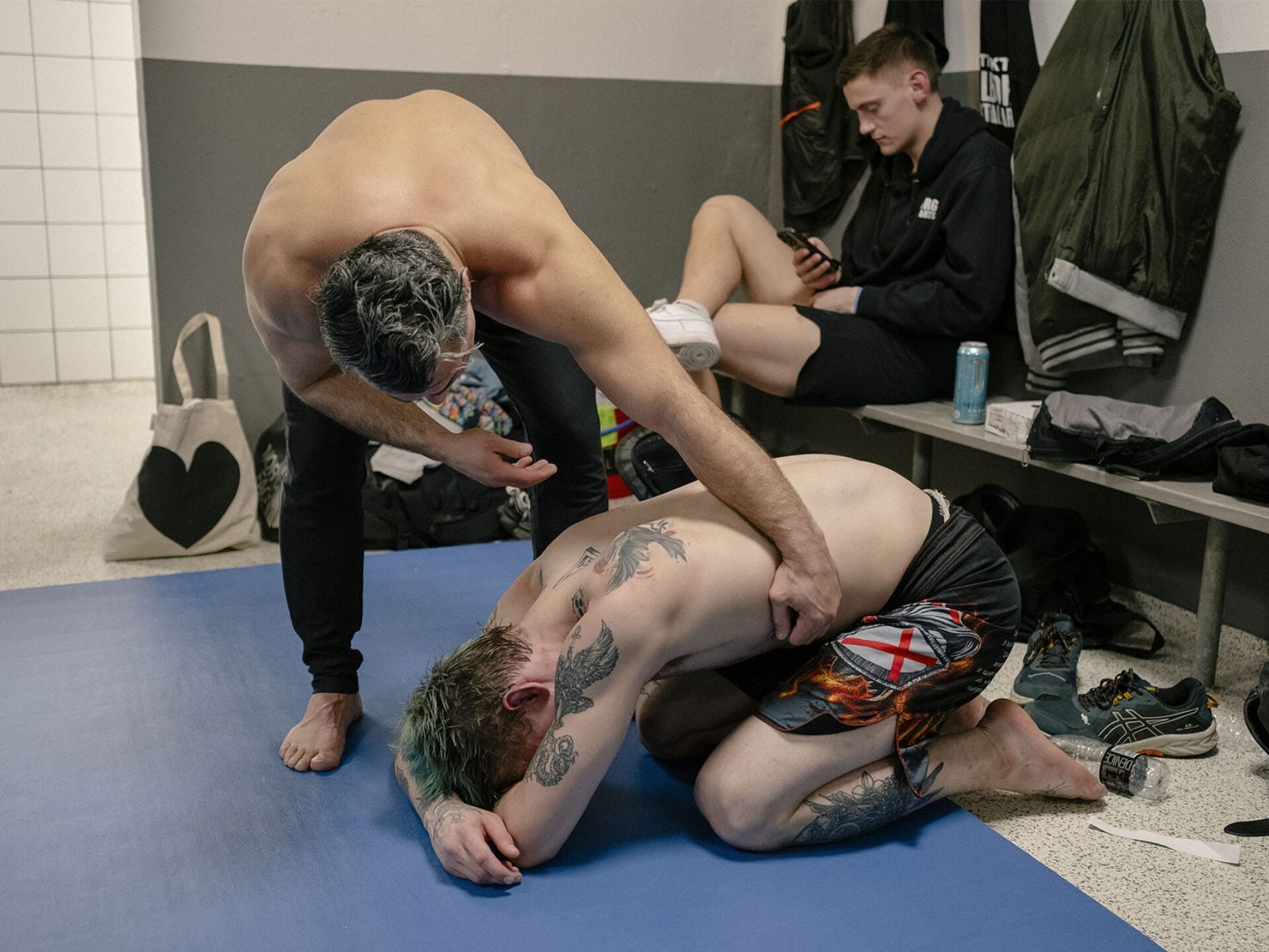 En MMA-udøver lægger en hånd på ryggen af en holdkammerat, der sidder sammenkrøbet på en måtte i omklædningsrummet.