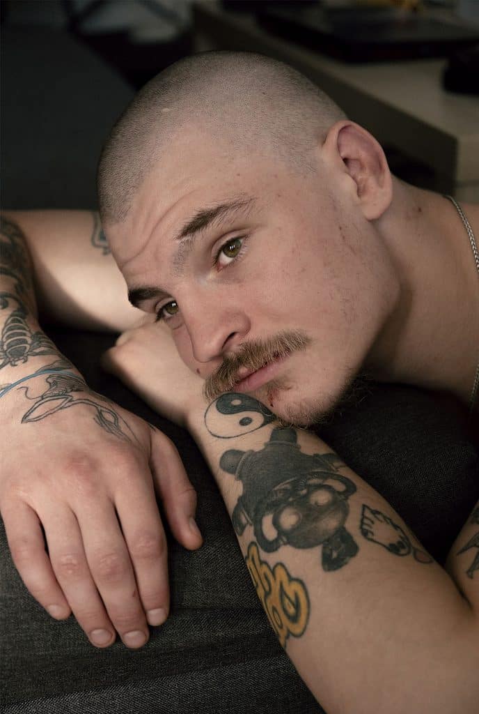 Patrick lægger med hovedet på sin arm og kigger fjernt ud i luften, forbi kameraet.