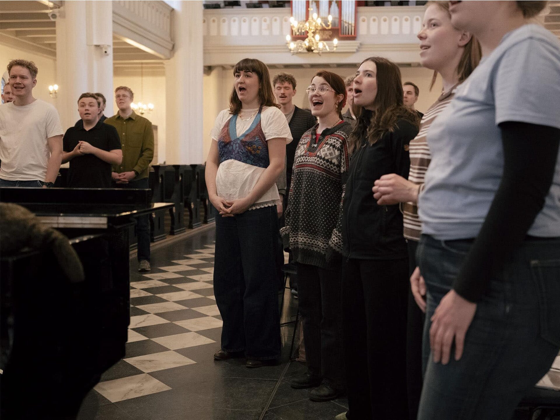 En stor gruppe unge mennesker står i en kirke og synger i kor